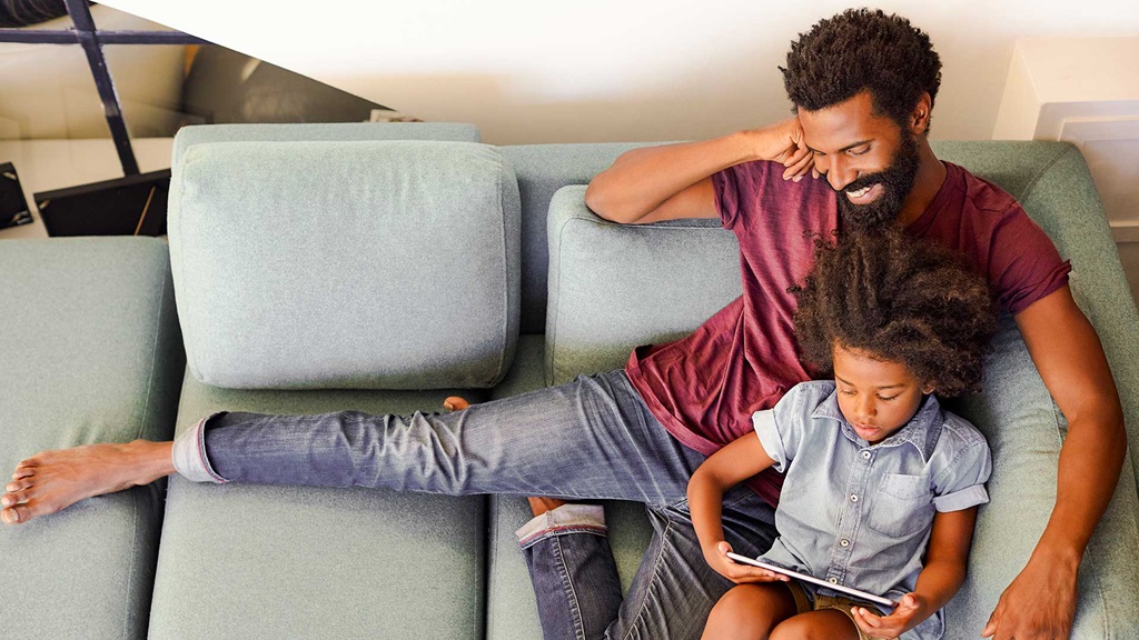 Father and child relaxing on a sofa reading a book
