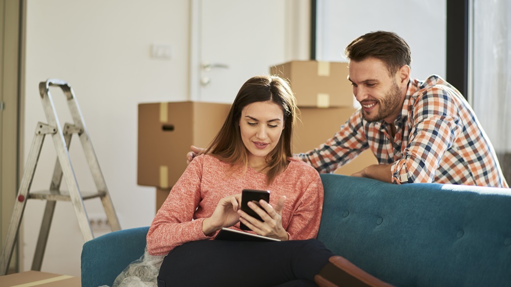 Couple checking a smartphone while surrounded by packing boxes
